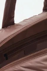Bolso marrón con diseño matelassé, doble asa corta, correa larga desmontable y dos bolsillos frontales. Incluye llavero de corazón y dijes desmontables.