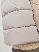 Chaleco acolchado sin mangas color gris claro, con cuello alto y cierre de cremallera. Tiene bolsillos frontales y forro de poliéster reciclado, con relleno de poliéster reciclado.