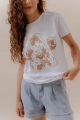 Remera blanca de algodón con calce relajado y estampa frontal de una flor grande con pétalos en tonos neutros y detalles en dorado.