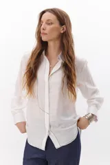 Camisa blanca de corte clásico con cuello camisero, manga larga y cierre frontal con botones. Presenta costuras a contraste en color negro.