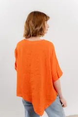 Blusa color naranja confeccionada en 100% lino, con escote en V, mangas cortas con vuelta y silueta amplia. Presenta terminación asimétrica y fila de botones decorativos en uno de los hombros.