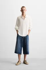 Camisa de hombre color blanco, de manga larga y cuello solapa, con un patrón jacquard sutil a cuadros. Presenta un calce relajado (relaxed fit) y bajo con aberturas laterales.