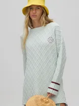 Sweater color crema con tejido en ochos, cuello redondo, puños acanalados con doble raya azul y tajos a los costados.
