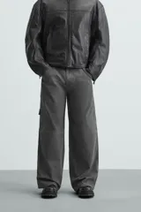 Pantalón de algodón color gris oscuro con efecto lavado, corte relaxed fit y pierna ancha. Presenta bolsillos delanteros, bolsillos traseros de plastrón y un bolsillo lateral con cierre de cremallera en la pierna.