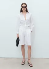 Camisa blanca oversize de lino, con cuello camisero, manga larga con puños abotonados y cierre frontal con botones.