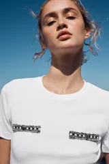 Camiseta blanca de corte slim fit, escote redondo y manga corta. Presenta apliques de fornitura a contraste en el delantero.
