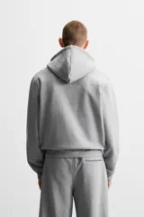 Sudadera negra relaxed fit de algodón compacto con interior en rizo, cuello con capucha ajustable, manga larga, bolsillos frontales tipo canguro, acabados en rib y cierre frontal con cremallera.