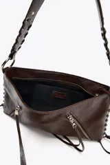 Bolso de hombro marrón de cuero sintético con dos bolsillos frontales con cremallera y tiras decorativas. El asa es trenzada y tiene herrajes metálicos.