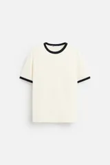 Camiseta color crema de corte recto, con cuello redondo y mangas cortas con ribete negro en cuello y mangas.