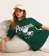 Remera verde de algodón con cuello redondo y mangas cortas. Estampa frontal con el logo de Peanuts y Snoopy jugando al tenis.