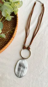 Collar de tiento marrón chocolate con dije ovalado de guampa y detalle en níquel.
