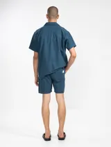 Bermuda de lino color marrón con bordado de flores blancas en la pierna izquierda. Tiene cintura elástica con cordón de ajuste, bolsillos laterales y un bolsillo trasero tipo parche.