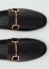 Mocasines negros de cuero con punta almendrada y detalle de hebilla dorada.