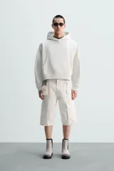 Sudadera con capucha color crudo, corte boxy, manga larga y bolsillo tipo canguro.