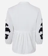 Blusa amplia de viscolino color blanco con bordados florales negros en mangas y escote, lazo en el cuello y mangas 3/4 con puño ajustado.