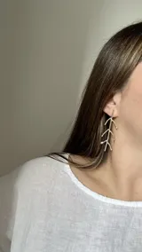 Caravanas largas de bronce con diseño de ramas o espigas en color dorado.