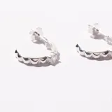 Par de caravanas plateadas con forma de medio aro con borde ondulado.