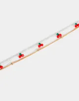 Pulsera flexible dorada con doble cadena, una de mostacillas transparentes y otra de metal, con dijes de cerezas rojas y verdes.