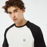 Camiseta blanca con mangas cortas raglán negras y logo pequeño en el pecho.