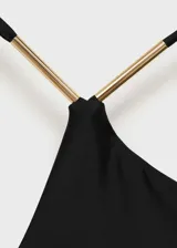 Traje de baño enterizo negro asimétrico con un solo tirante fino y detalle metálico dorado en el hombro.