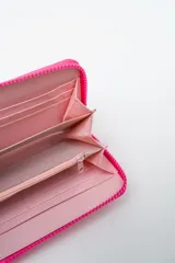 Billetera rectangular color fucsia con cierre perimetral y parche frontal negro con logo. Incluye correa de mano de cordón rosa neón y detalle de ajuste en verde lima.