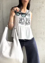 Blusa blanca sin mangas con bordado floral negro en el frente, corte evasé y cierre frontal con botones.