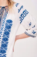 Vestido túnica blanco con bordados azules, mangas 3/4 y cuello con lazo ajustable.