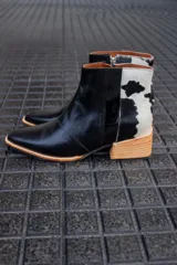 Bota corta de cuero negro con panel trasero de cuero vacuno blanco con manchas negras. Tiene cierre lateral y taco de madera.