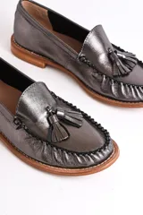 Mocasines de cuero color marrón claro con detalle de borlas en el empeine y costuras decorativas.