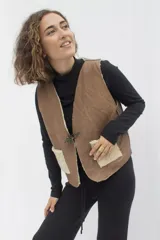 Chaleco marrón de cuero con interior de corderito color crema, cierre con gancho metálico y bolsillos frontales de corderito.