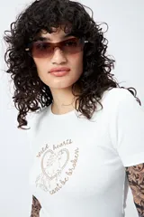 Remera color beige con cuello redondo y mangas cortas. Presenta un estampado con relieve de un corazón con un caballo en su interior y la frase "wild hearts can't be broken".