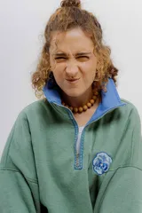 Buzo verde con cuello polo azul y cierre metálico parcial. Presenta un bordado de una flor en el pecho.