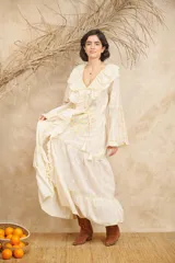 Vestido largo color crema con bordados florales en tonos pastel, escote en V con volados, mangas largas acampanadas y abertura frontal. Incluye lazo ajustable en la cintura.