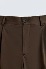 Pantalón relaxed fit color marrón confeccionado en tejido de algodón con estructura twill. Cintura con pliegues frontales, bolsillos laterales en cadera y detalle de bolsillos traseros de doble vivo con botón. Cierre frontal con cremallera y botón.