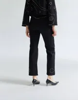 Pantalón de denim negro con corte recto y tachas plateadas decorativas.