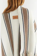 Ruana artesanal color beige con rayas horizontales rojas y amarillas, y flecos en el borde inferior.