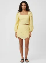 Short pollera color amarillo pálido con bordado de puntilla, corte mini y cierre lateral oculto.