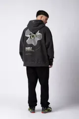 Buzo canguro negro con capucha, de corte oversize y estética lavada. Presenta un bolsillo tipo canguro y puños con orificio para el pulgar. Estampado con texto en el lateral izquierdo.