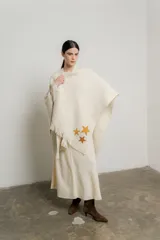 Ruana color crema de tejido grueso con flecos y apliques de estrellas doradas.