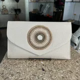 Sobre de fiesta color crudo, tejido artesanalmente en la India. Tiene aplique central bordado con mostacillas, cristal e hilo en tonos dorados y crudo. Incluye asa de cadena dorada para colgar del hombro.