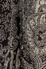 Camisa de viscosa con estampado paisley en blanco y negro, cuello redondo con volantes y escote pico ajustable con cordones. Mangas largas con elástico y volantes en los puños, bajo asimétrico y cierre frontal con botones forrados.