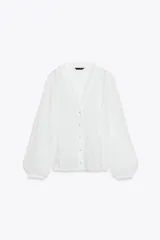 Blusa blanca de manga larga con escote en pico, detalle de tejido con frunces, entredoses y plumeti. Cierre frontal con botones.