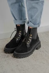 Borcego de gamuza color negro con cordones y herrajes metálicos. Cuenta con elásticos laterales que facilitan el calce y suela track.