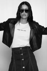 Remera blanca de algodón con la frase "enjoy the now." estampada en negro. Tiene cuello redondo y mangas cortas.