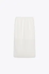 Falda midi color blanco, semitransparente, de tiro medio con cintura elástica, forro corto interior y abertura en la espalda.