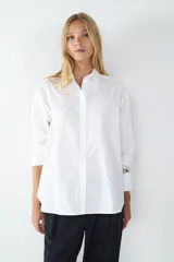 Camisa blanca de popelina de algodón, de corte amplio, manga larga, cuello clásico, cierre frontal con botones y puños abotonados.
