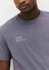 Camiseta blanca de algodón con cuello redondo y mangas cortas. Estampa rectangular con borde negro que contiene la frase "NATURAL ATMOSPHERE" en letras mayúsculas y una imagen de montañas y mar.