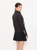 Camisa negra de poplin con bordado de chiles rojos, cierre frontal con lazos, broches decorativos dorados en el cuello y broches a presión dorados en los puños.