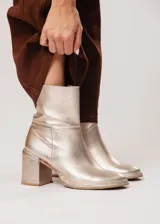 Bota de caña media color champagne de cuero, con horma redonda, taco cuadrado y pequeña plataforma. Cuenta con cierre del lado interno.
