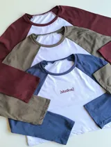 Remera corta blanca con mangas largas azul marino y logo "[studios]" estampado en rojo.